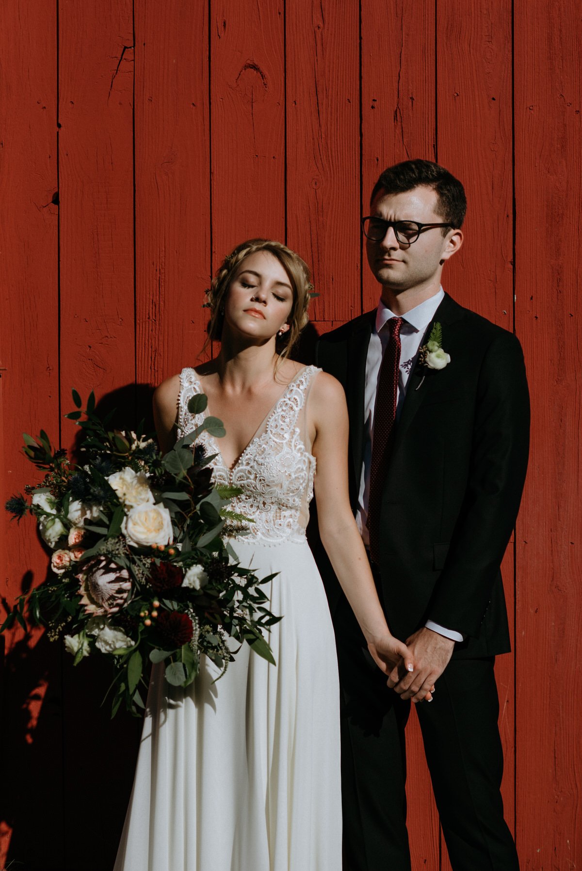 bride and groom posed in front of red barn