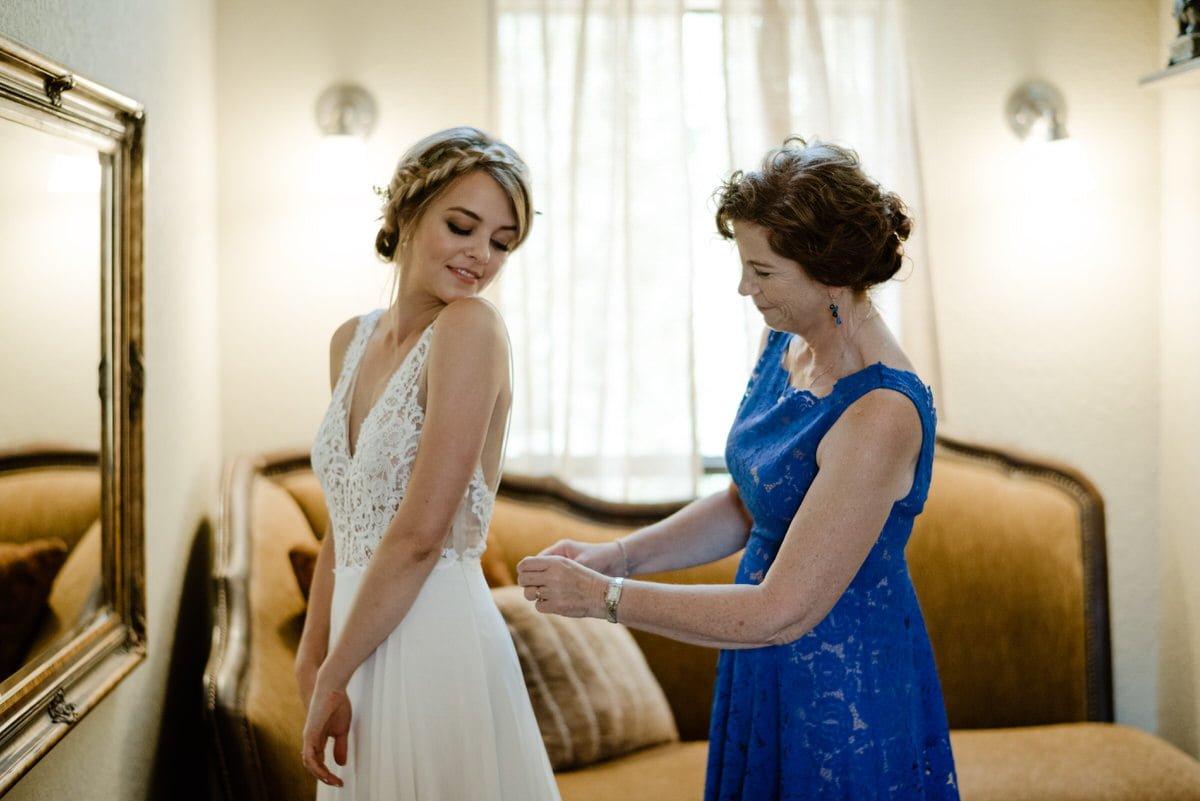 mother helping bride put on dress