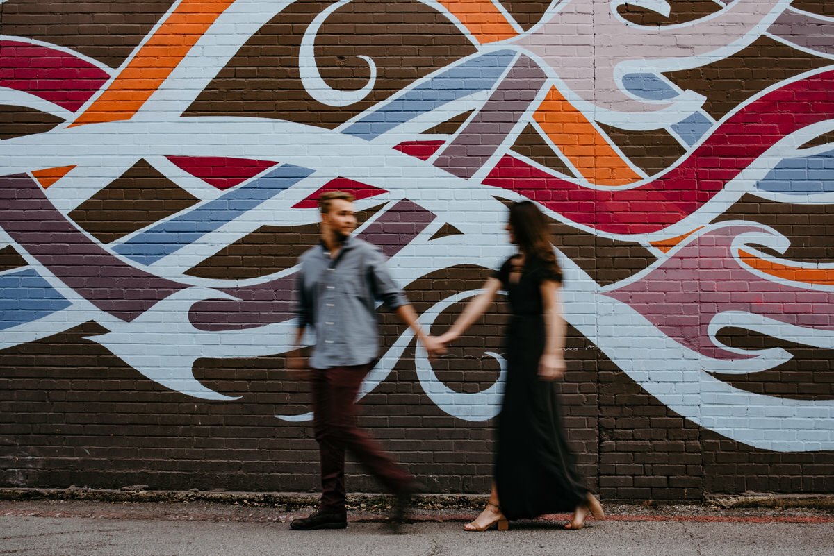 motion shot of couple walking in front of colorful wall