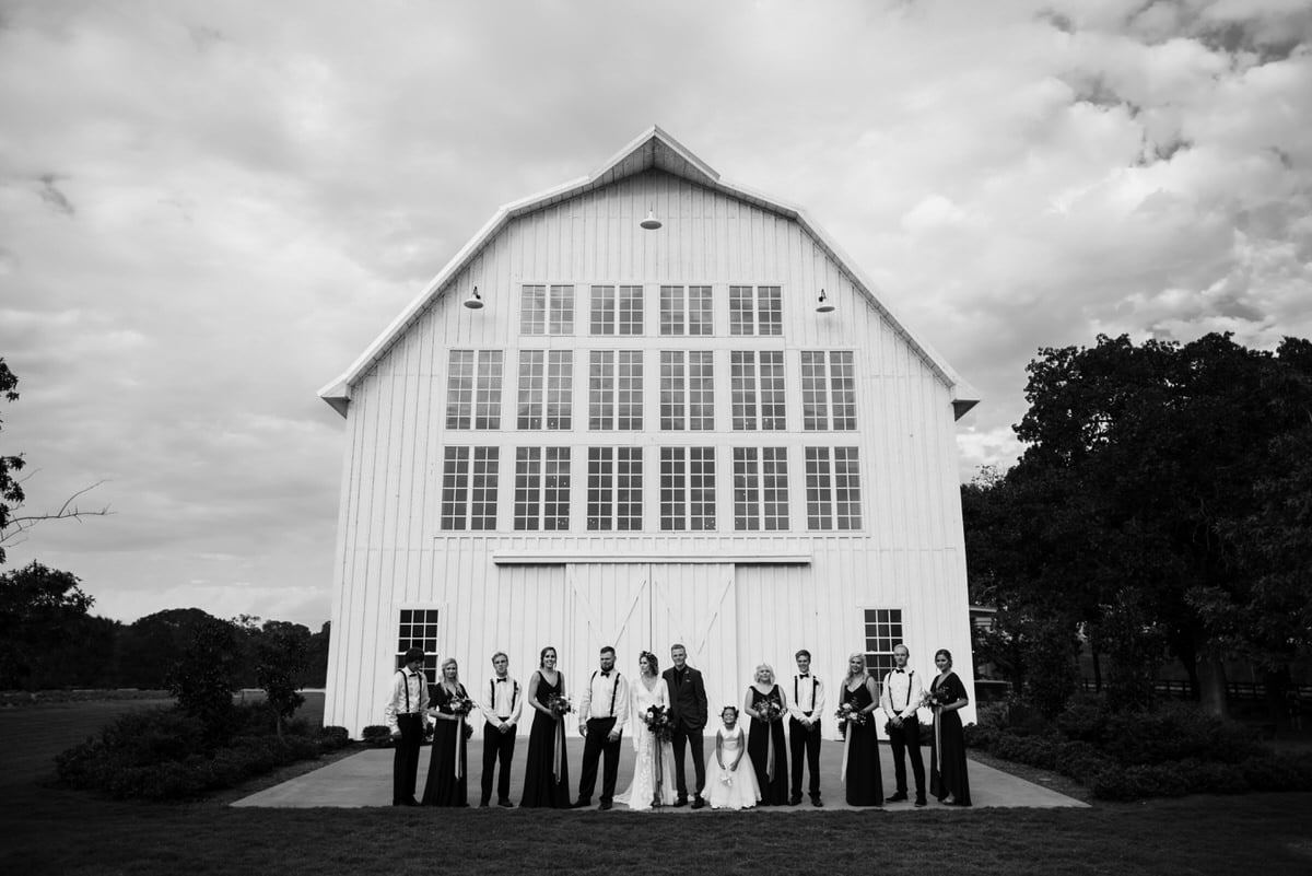 bridal party posed in front of large barn