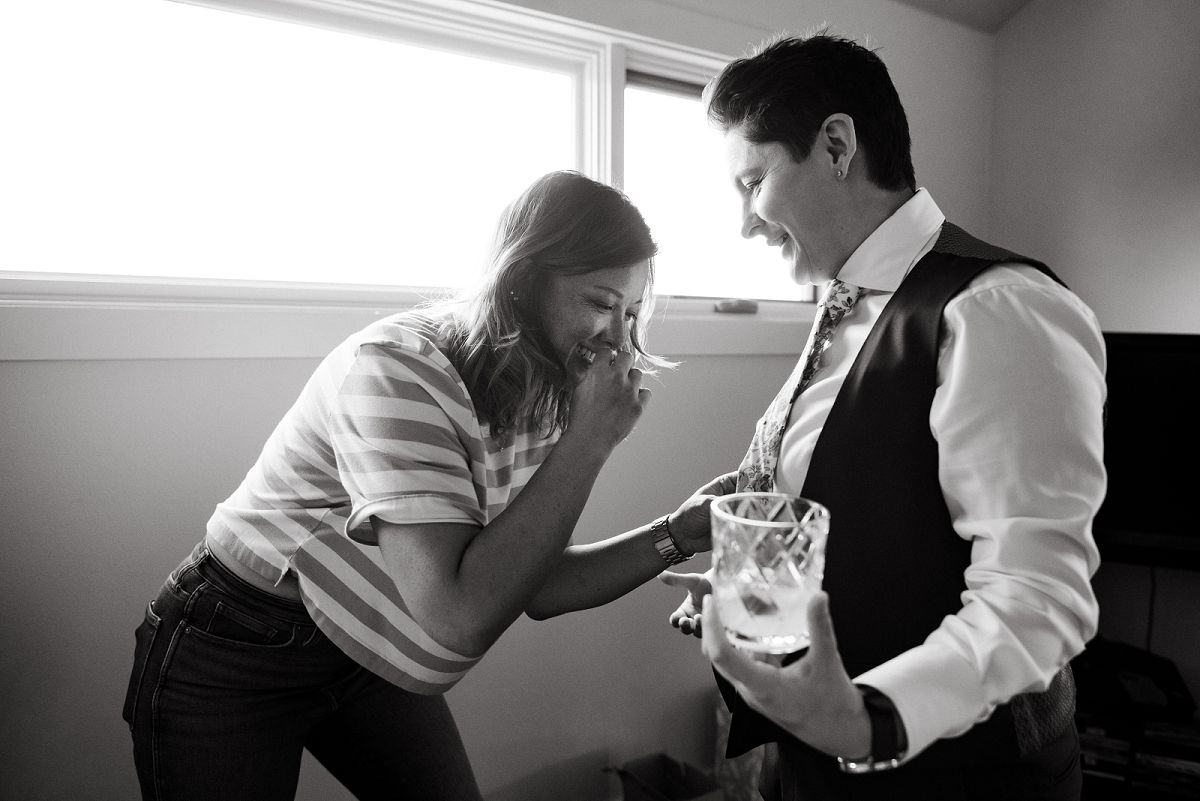 bride getting ready in suit smiling holding a glass of whiskey