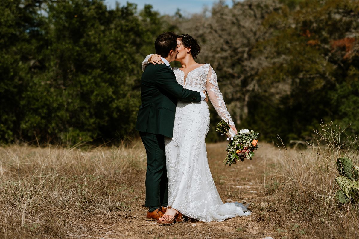 same sex couple kissing at wedding in field