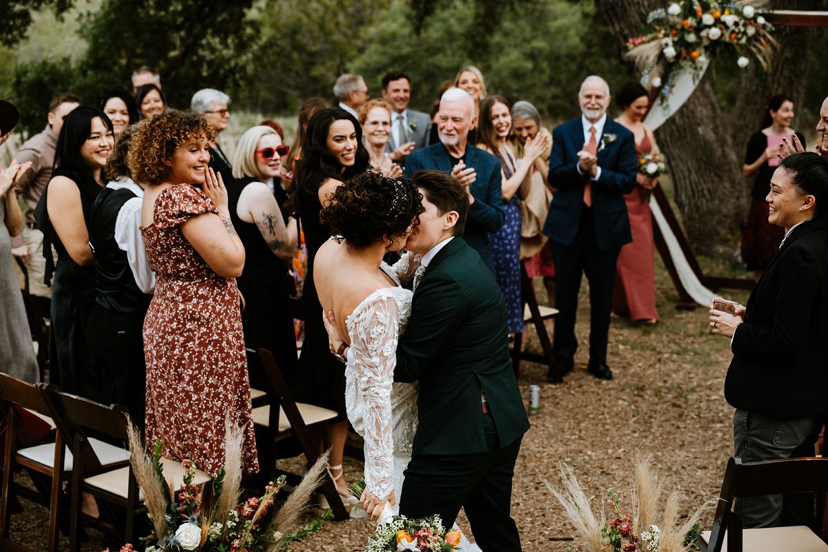 brides kissing at end of aisle in front of guests