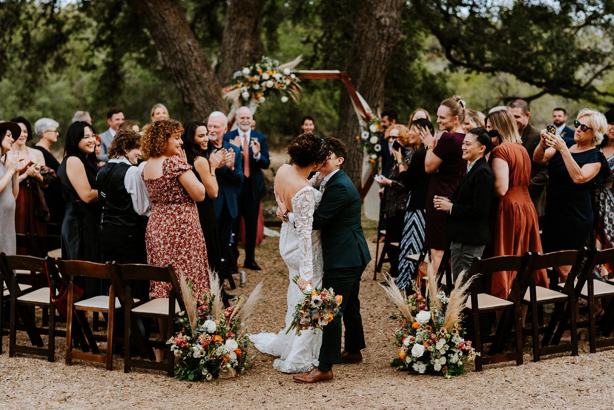 brides kissing at end of aisle in front of guests