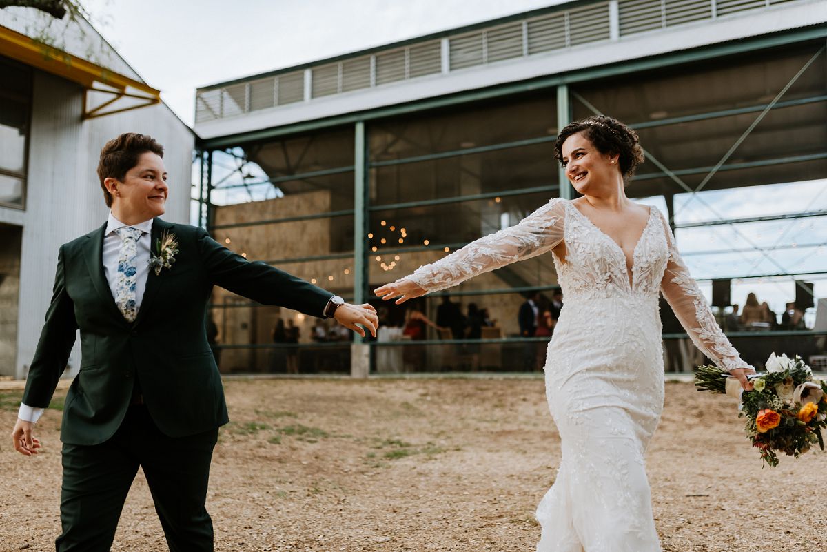 brides walking with arms stretched out towards each other smiling