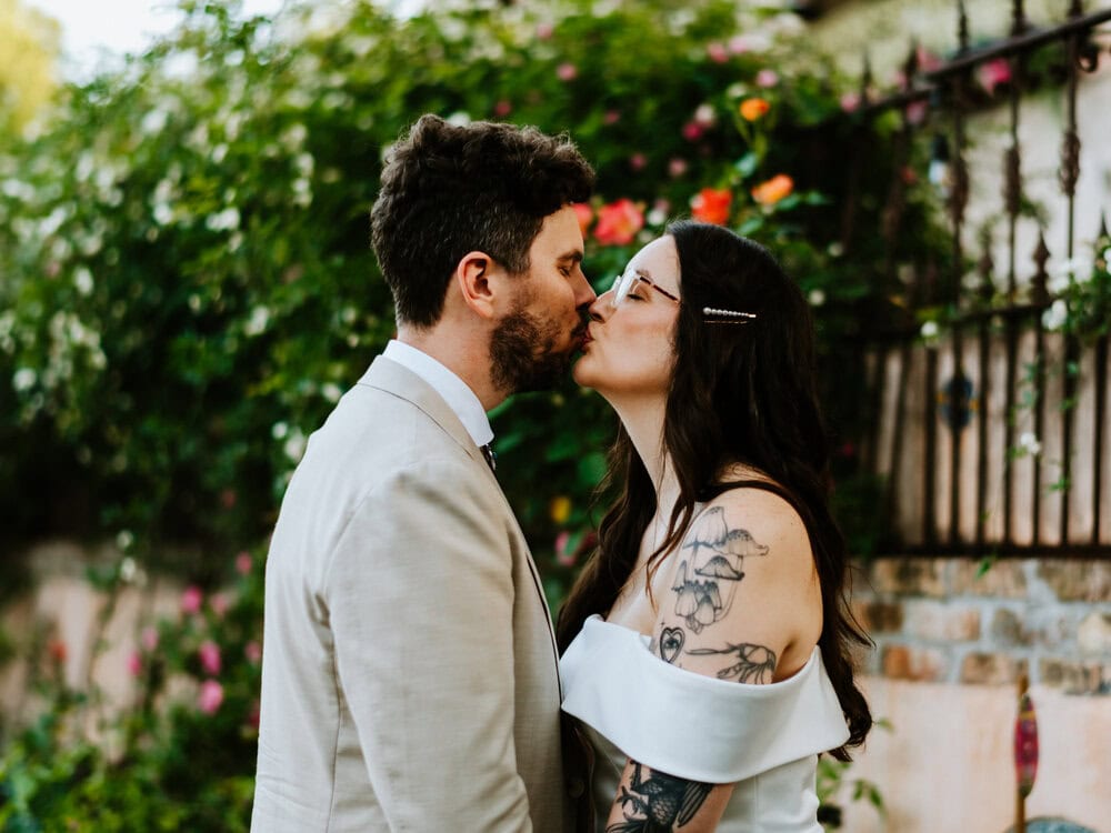 couple kisses in front of pink blooming bush