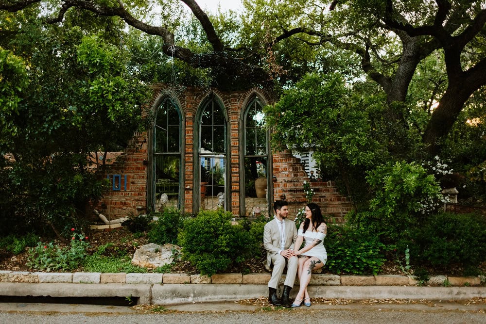 wide photo of couple sitting on curb in front of artistic building with unique pointed windows