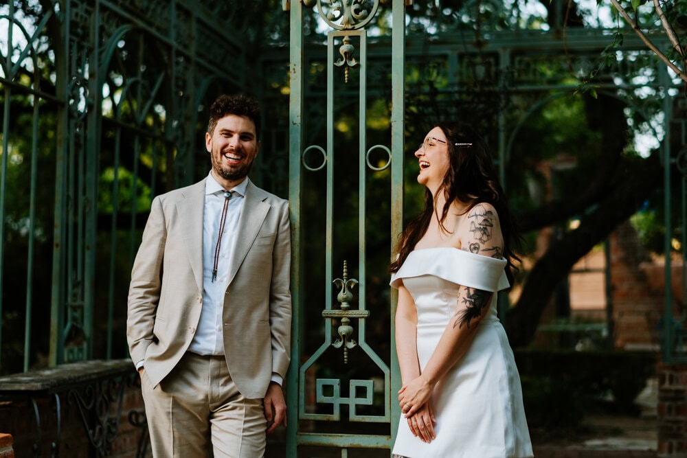 couple leans on metal bars of building frame smiling