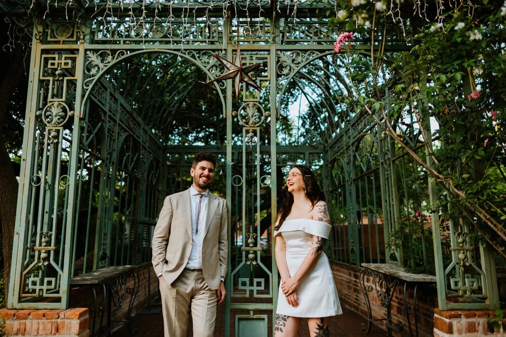 couple leans on metal bars of building frame smiling