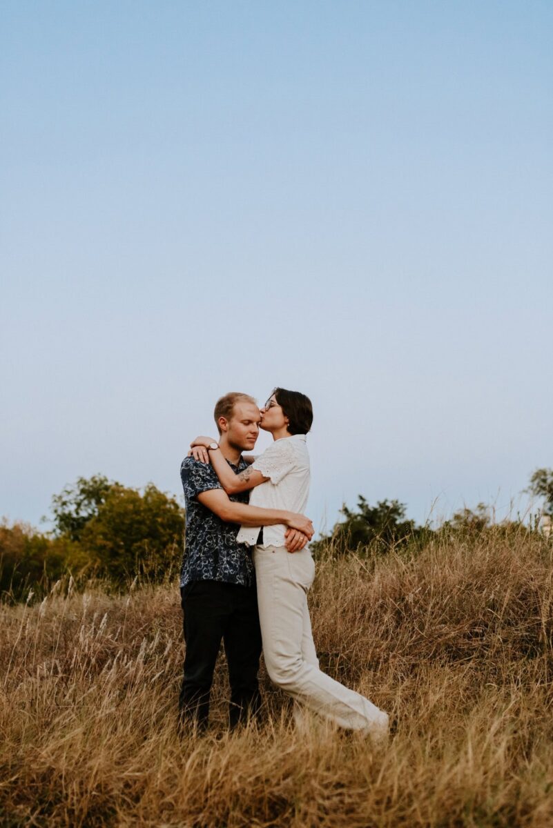 couple holding each other kissing in field during sunset