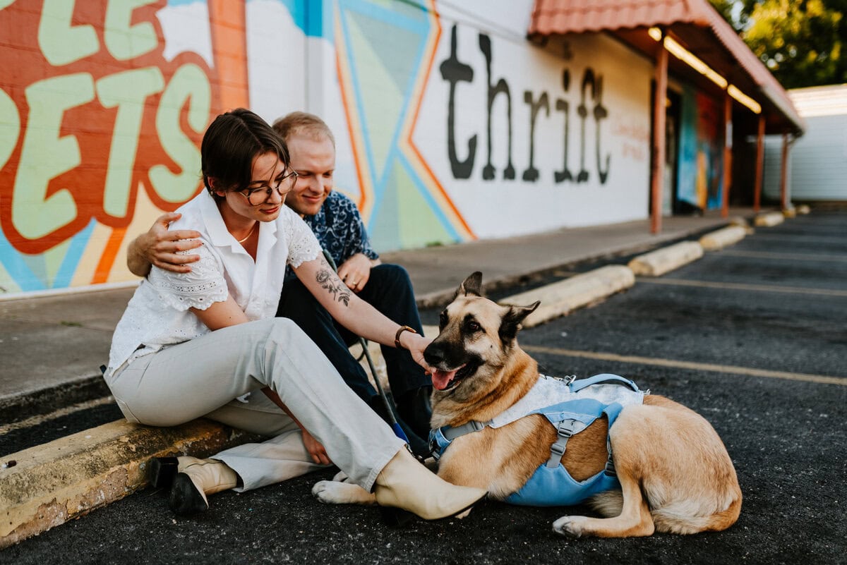 couple sitting with dog in front of mural