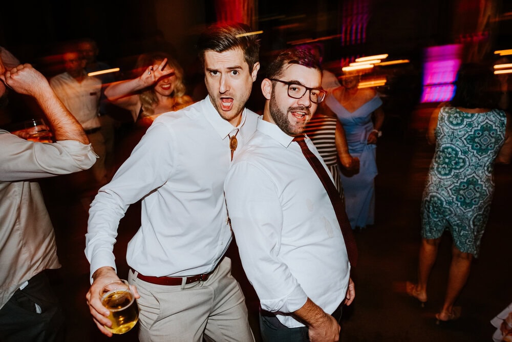 two guys leaning in posing for camera during wedding reception