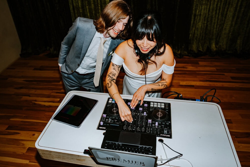 bride and groom smiling behind dj table during surprise set at their wedding