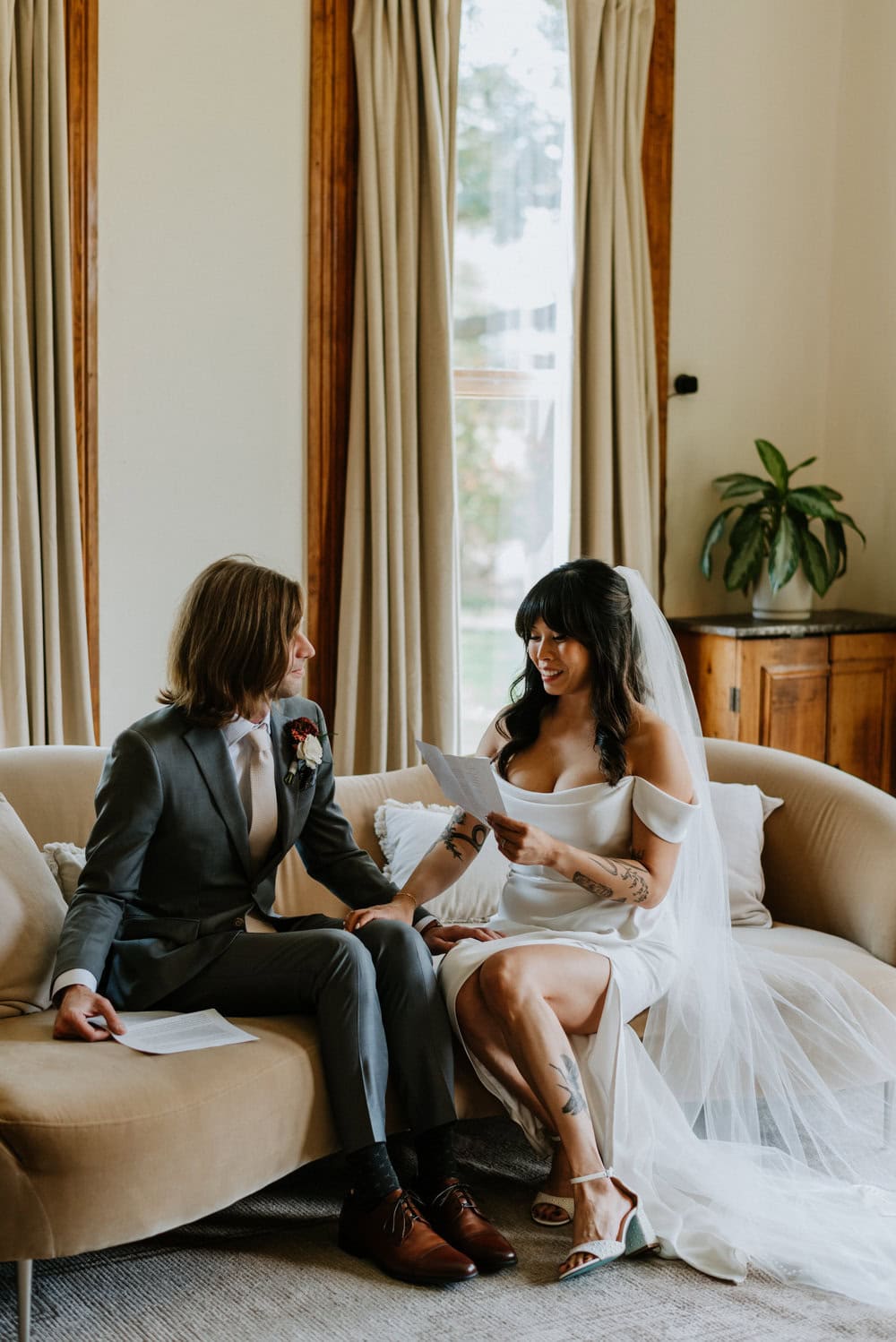 couple sits on couch while bride reads private vows to groom