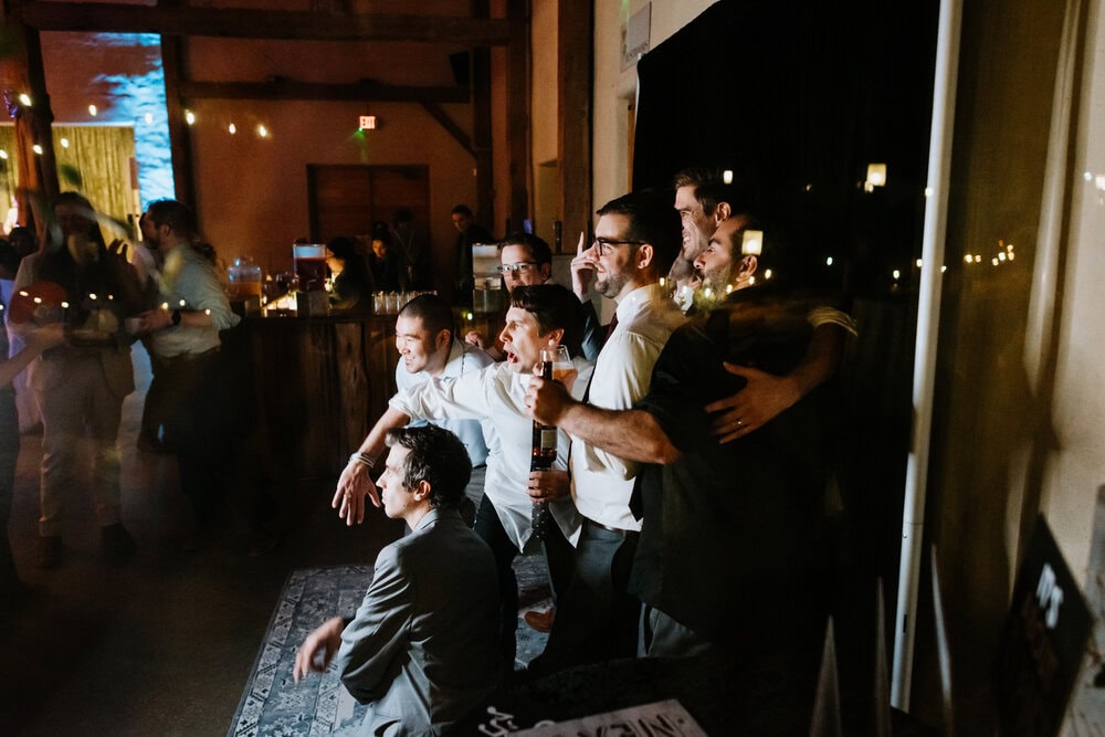photo through window showing groom and guys posing in front of photo booth at wedding reception
