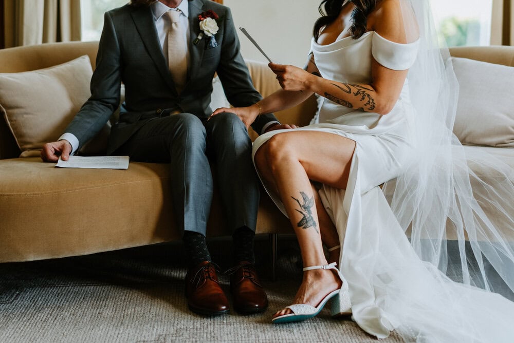 detail photo of bride holding grooms knee while reading private vows showcasing her tattoo on leg