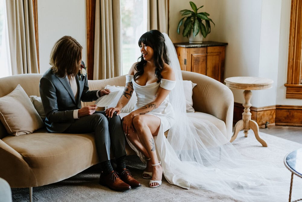 groom reads bride vows while they sit on couch indoors