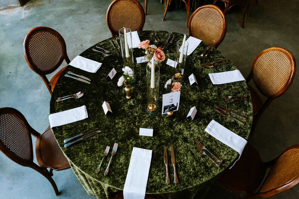 photo from above wedding reception table with green velvet table cloths, candles, and warm tone florals