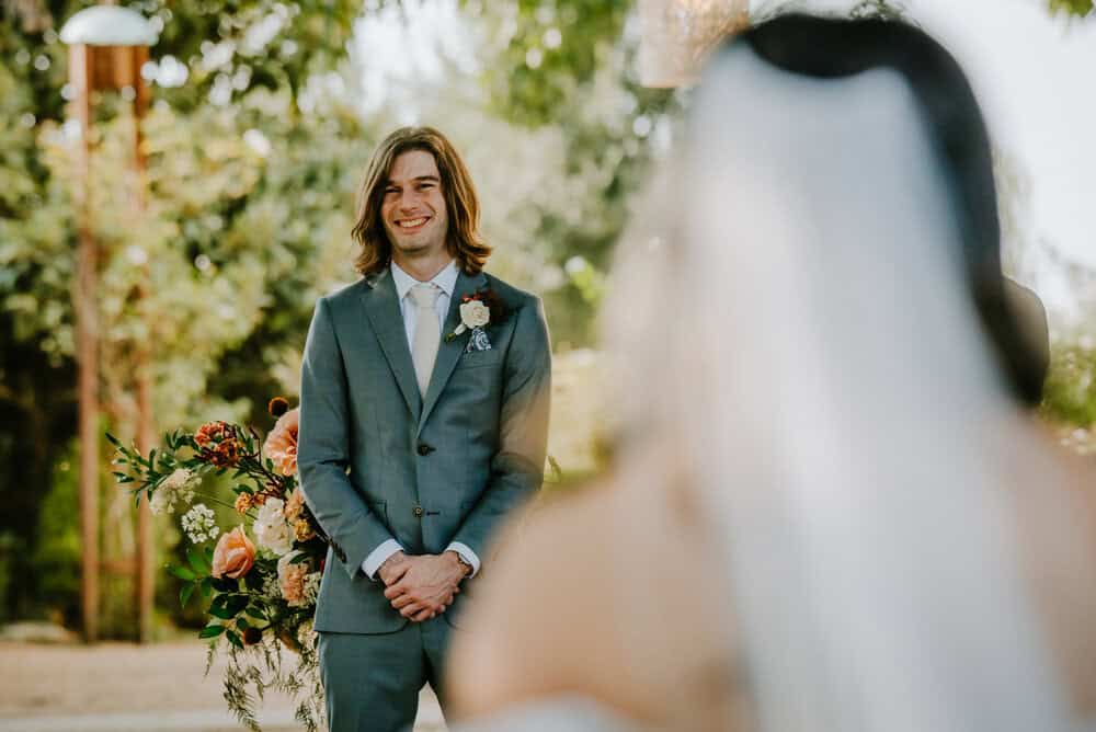 photo of grooms reaction through brides veil as she walks down aisle