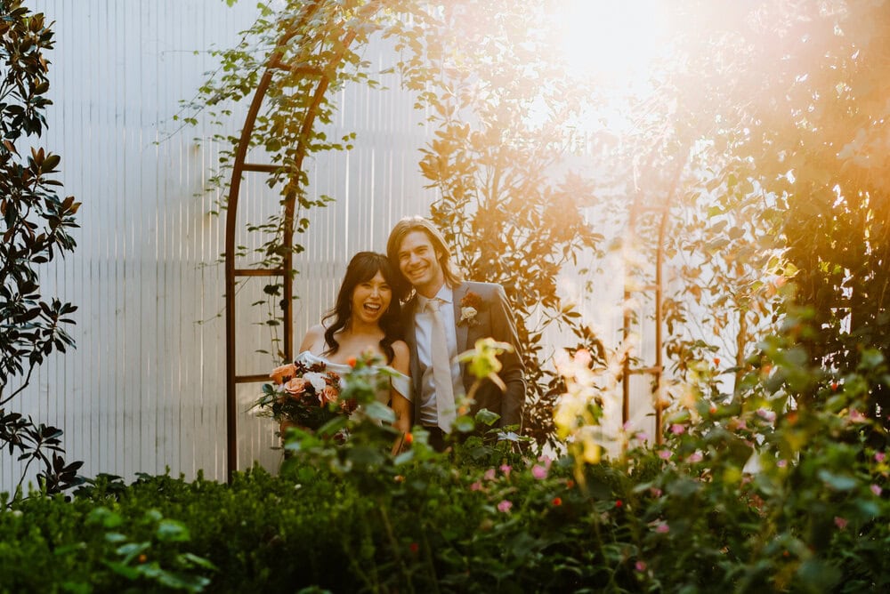 couple poses next to each other in garden with florals and sunlight