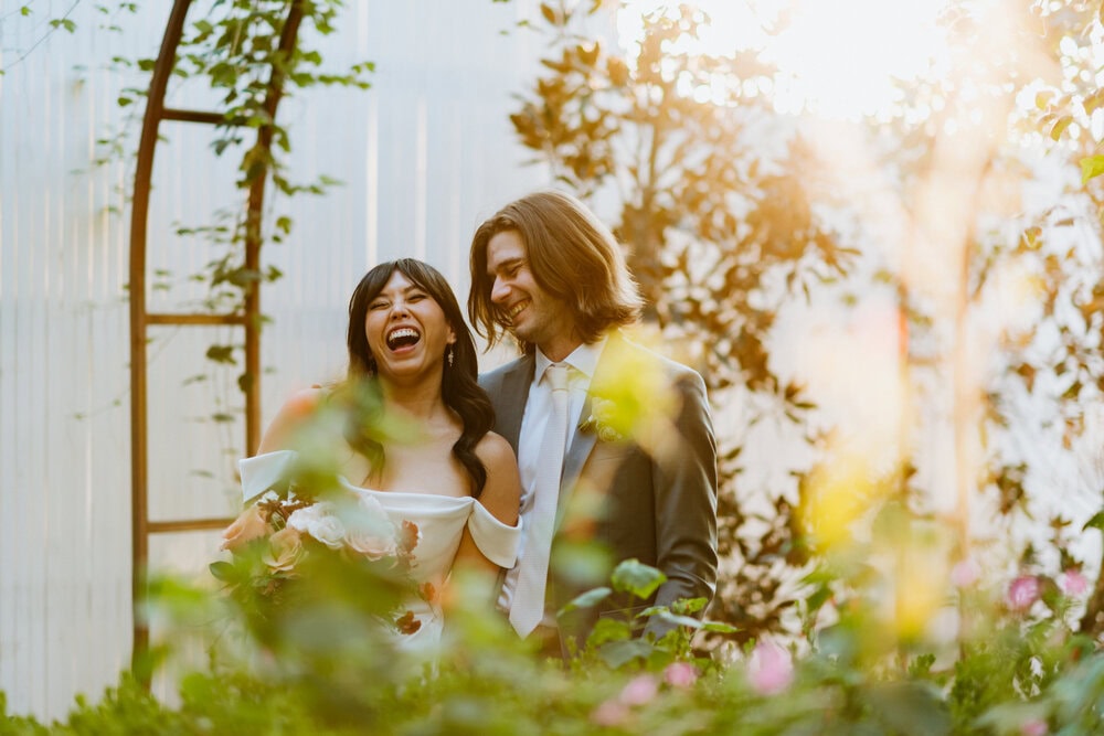 couple poses next to each other in garden with florals and sunlight