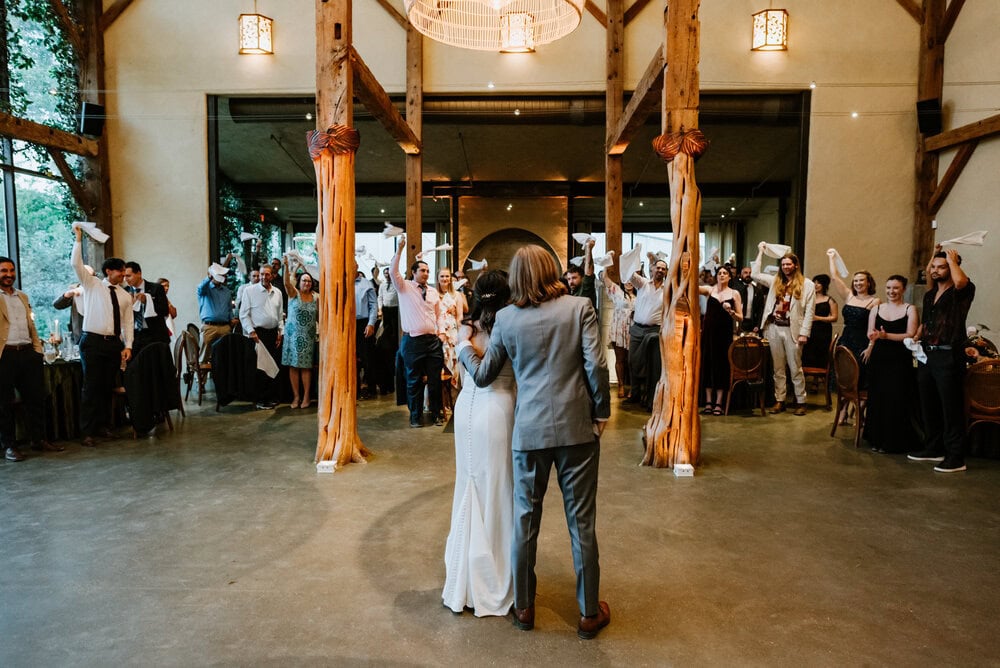 back photo of couple standing in front of wedding guests at reception waving