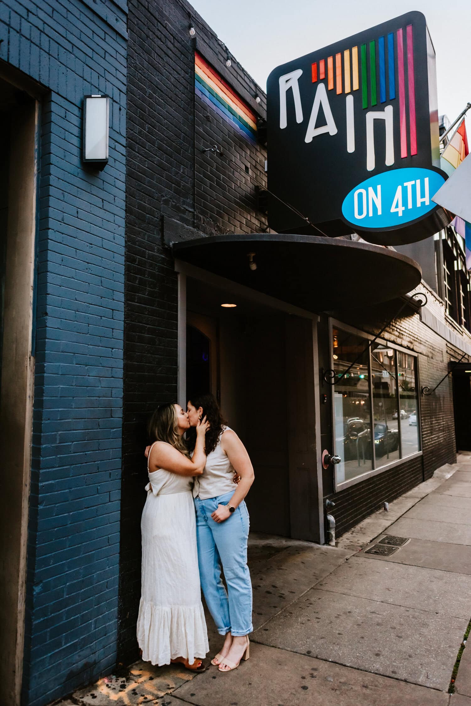 lesbian couple stands kissing in front of rain sign in downtown austin